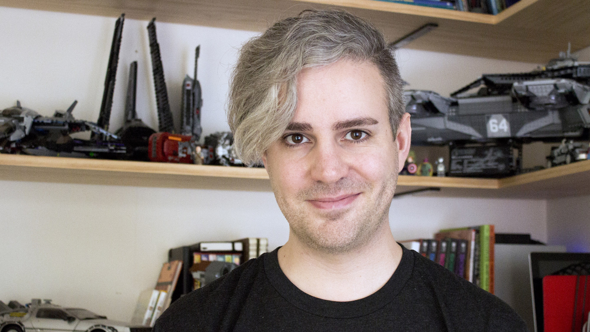 A portrait of Daniel Farrelly, standing in front of shelves that contain Lego, books and a model Delorian